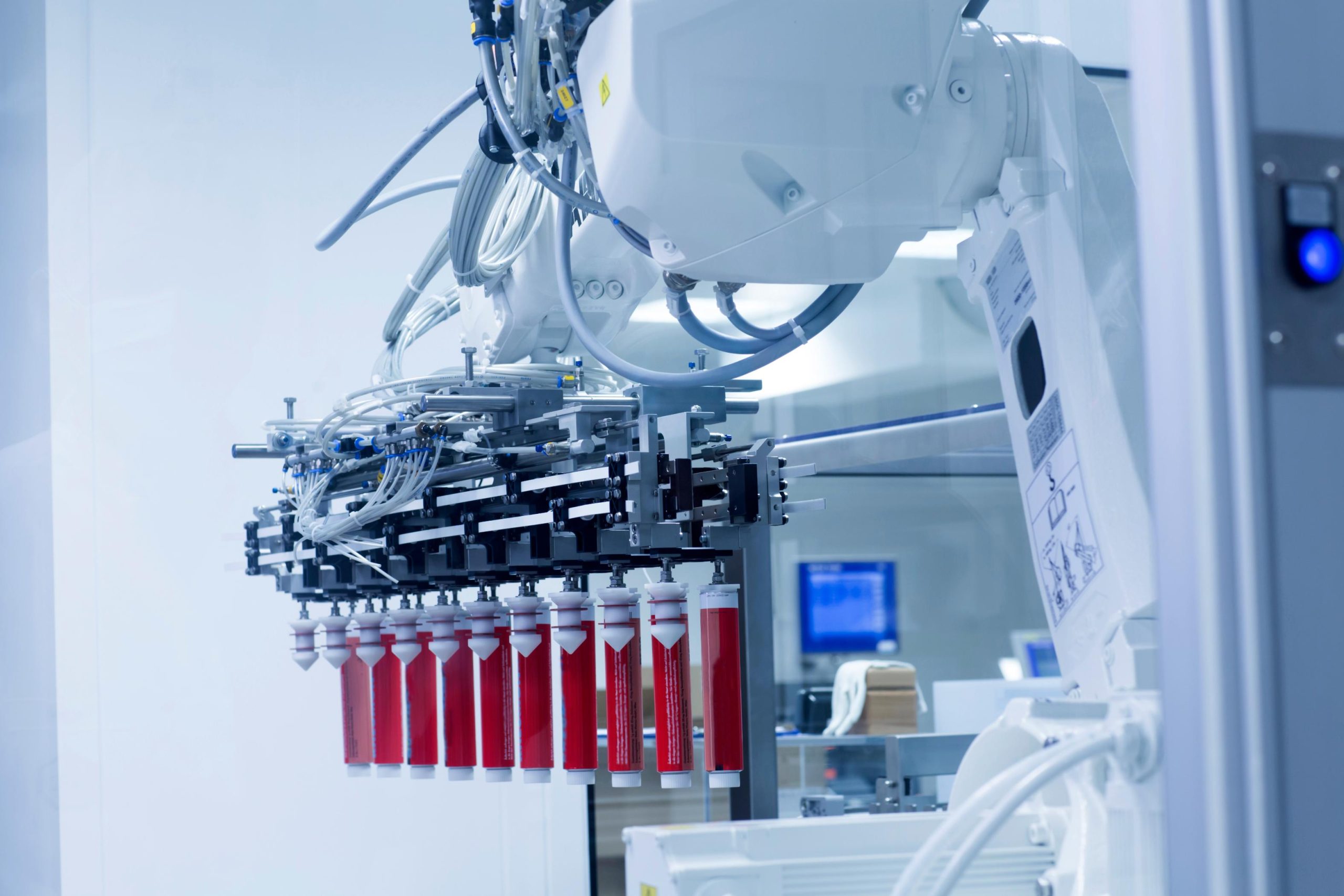 Robot industrial automatizado manipulando tubos farmacéuticos en línea de producción con sistema de inspección y control de calidad.